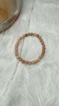 Peach moonstone bead stretch bracelet with round tan beads, laid on light fabric